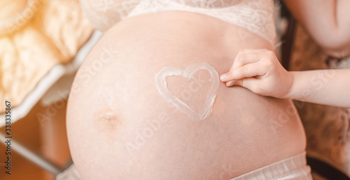 Wallpaper Mural Heart shape painted with creme on belly of pregnant woman. Closeup of pregnant woman holding her belly Torontodigital.ca