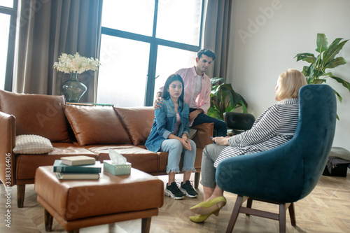 Dark-haired tall man and his girlfriend sitting on the sofa talking to the psychologist