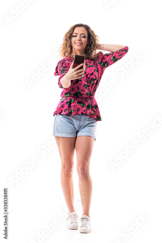 Summer beauty curly hair girl taking self portrait with cell phone touching hair and smile. Full body isolated on white background. 