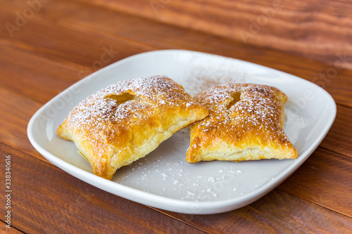 Sweet buns sprinkled with powdered sugar and cinnamon on white plate on wooden table. Freshly baked bakery product, side view, close-up.