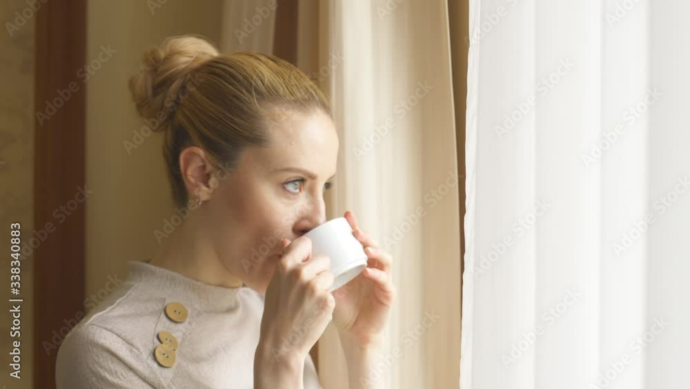 Woman before a working day in morning drinks coffee by window and looks out Woman before a working day in morning drinks coffee by window and looks out