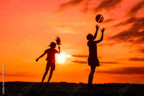 Silhouettes of playing boy with windmill and girl with ball in the nature in cloudy sky background