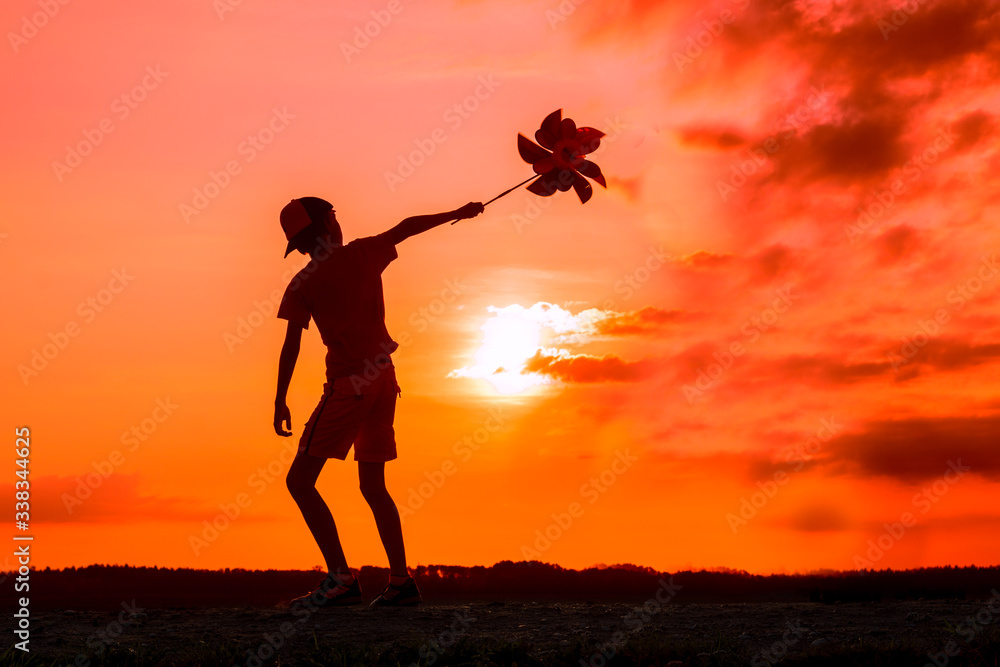Silhouette of playing boy with windmill  in the nature in cloudy sky background