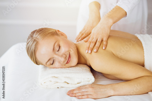 Beautiful caucasian woman enjoying back massage sunny spa salon. Beauty concept