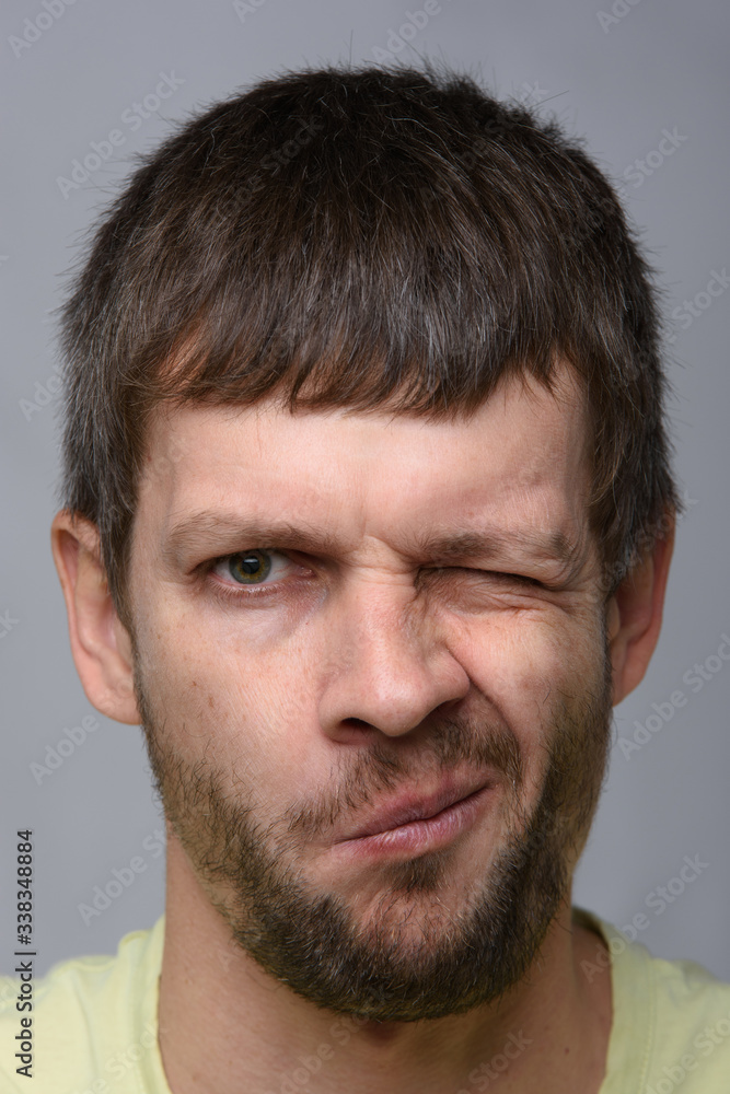 Close-up portrait of a man of European appearance who squeezed his right eye tightly Close-up portrait of a man of European appearance who squeezed his right eye tightly