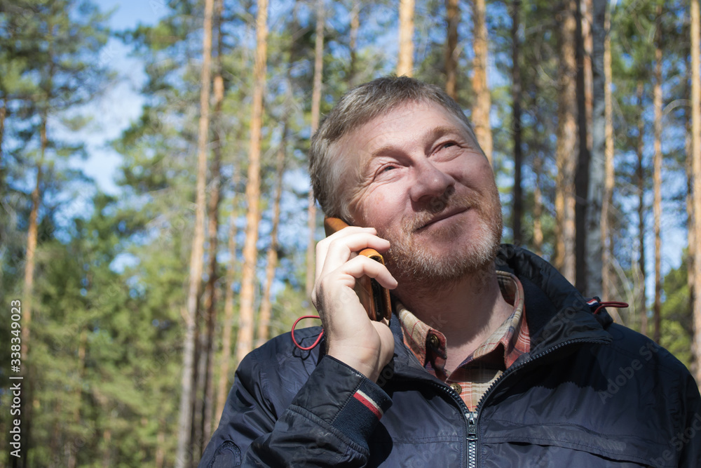 A middle-aged man smiles and talks on the phone in the park.