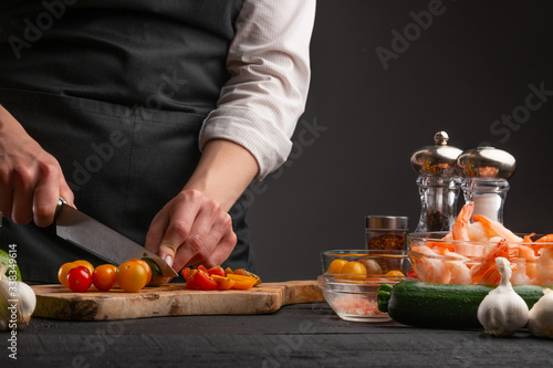 Cooking StirFry vegetables with shrimp. Chef slices cherry tomatoes, on a gray background with shrimp. Seafood
