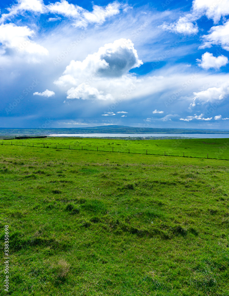 green field with sea in background in Ireland, blue sky with clouds