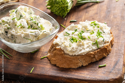 A bowl of homemade cream cheese spread with chopped chives surrounded by bread slices with spread and a bunch of freshly cut chives