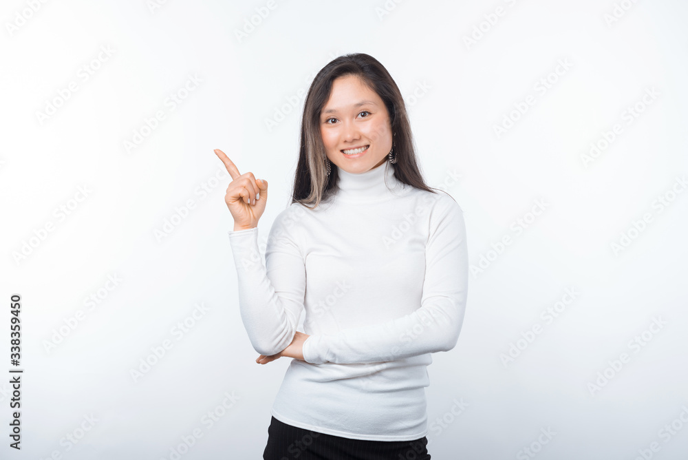 Photo of smiling girl wearing white is pointing up on a light background. Photo of smiling girl wearing white is pointing up on a light background.
