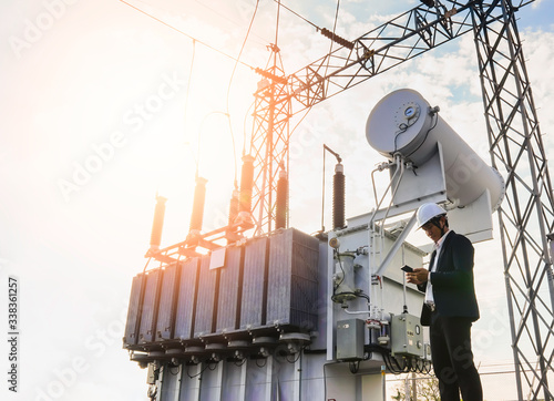 A low angle image of a businessman wearing a black suit, standing looking at a large power transformer with blue sky to be background, Concept about business people who want to invest in energy photo