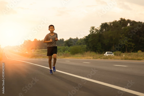 a boy comes to jogging in the evening on the public road on a holiday with the orange light of the sun coming from behind  leisure activities that make the body healthy