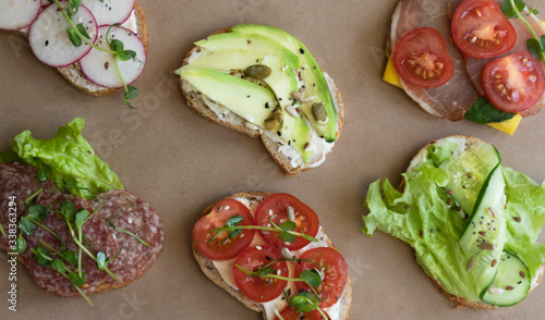 Close-up of sandwiches or tapas with avocado, cucumbers, meat, cheese, radish decorated with micro-greens and chia seeds, flax seeds and seeds, flat lay