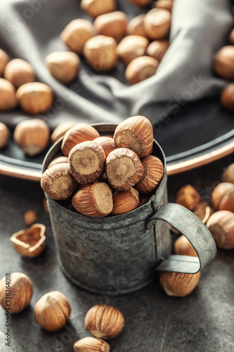 Hazelnuts and their cracked shells on a vintage dark metallic background, in a metallic cup and on a tray with a cloth