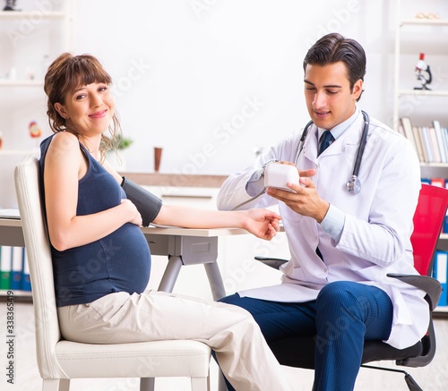 Young doctor checking pregnant woman s blood pressure