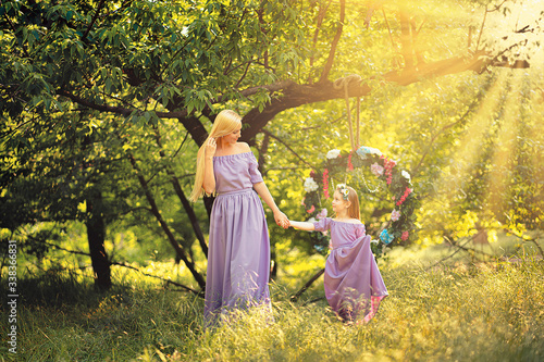 fashion outdoor photo of beautiful family look. beautiful mother with long blonde hair posing and playing with her daughter in similar lavender dresses in the park outdoor photo