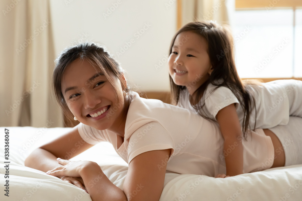 Vietnamese family play while lying on bed in warm cozy bedroom, little adorable daughter and asian beautiful mother relish time together wear comfortable pyjamas woke up enjoy new day feels overjoyed Vietnamese family play while lying on bed in warm cozy bedroom, little adorable daughter and asian beautiful mother relish time together wear comfortable pyjamas woke up enjoy new day feels overjoyed