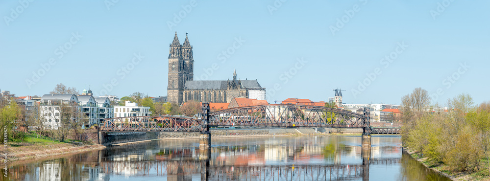 Panoramic cityscape of old railway metal rusty bridge over Elbe river in downtown of Magdeburg and cathedral at early Spring, Germany, sunny day, blue sky