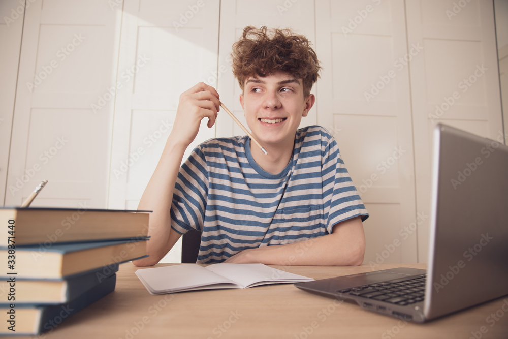 A smiling teenage boy learns at his desk in his room. Distance learning because of the epidemic coronavirus A smiling teenage boy learns at his desk in his room. Distance learning because of the epidemic coronavirus