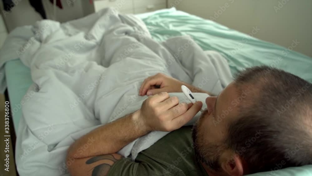 Man laying in bed being sick checking his temperature Man laying in bed being sick checking his temperature