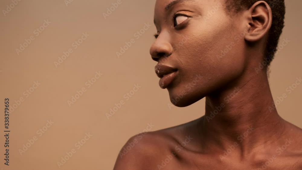 Close up view of Smiling pretty half-naked african woman with short black hair posing and looking away over beige background Close up view of Smiling pretty half-naked african woman with short black hair posing and looking away over beige background