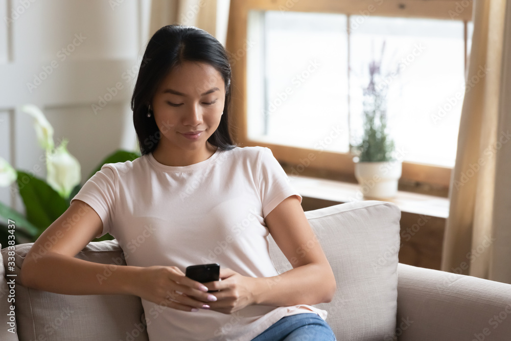 Absorbed Asian millennial woman resting seated on couch in cozy living room alone, using smart phone communicating with friends, read the latest media news, spend free time on-line in internet concept Absorbed Asian millennial woman resting seated on couch in cozy living room alone, using smart phone communicating with friends, read the latest media news, spend free time on-line in internet concept