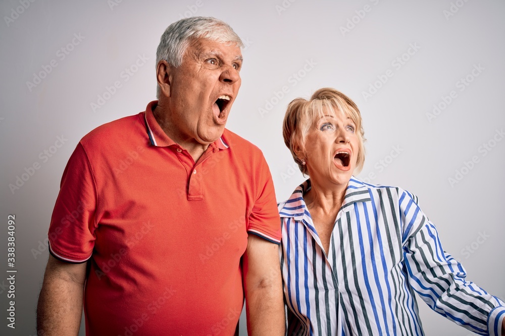 Senior beautiful couple standing together over isolated white background angry and mad screaming frustrated and furious, shouting with anger. Rage and aggressive concept. Senior beautiful couple standing together over isolated white background angry and mad screaming frustrated and furious, shouting with anger. Rage and aggressive concept.