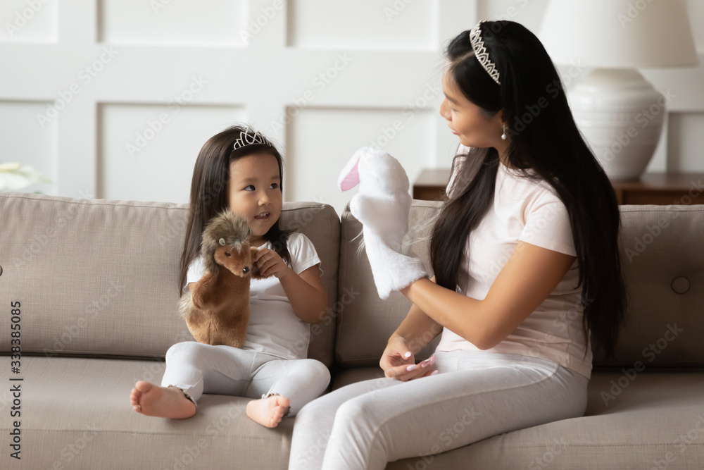 Φωτογραφία Vietnamese loving mother and toddler daughter wearing crowns casual clothes sit on couch playing with hedgehog and hare animal hand puppet toys