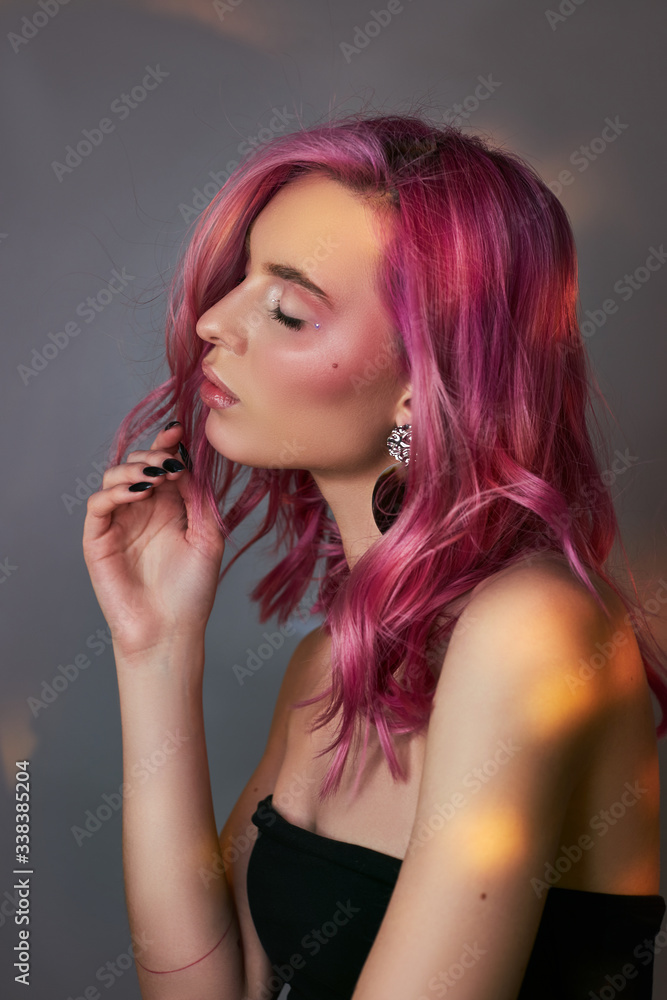 Fototapeta premium Art beauty portrait of a woman with pink hair, creative coloring. Bright colored highlights and shadows on the face, a girl with jewelry. Dyed hair in the wind