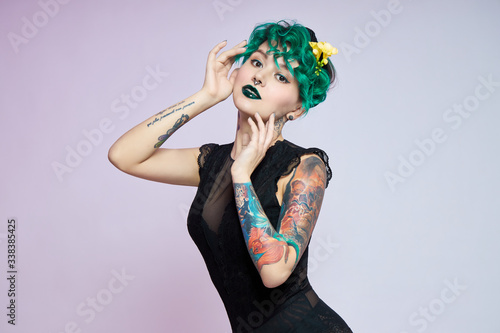 Woman with creative green coloring hair and makeup, toxic strands of hair. Bright color curly hair on the girl head, professional makeup. Woman with tattoo photo