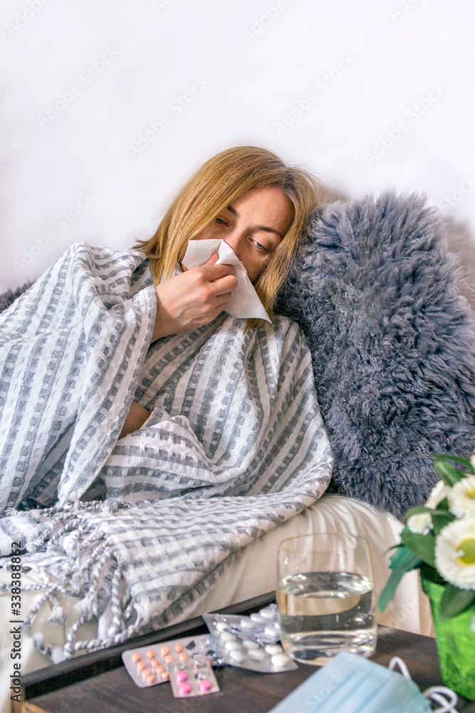 Fotografie Ill sick woman lies in bed blowing her nose, coughing