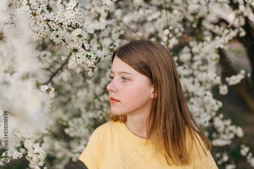 portrait of sad young woman in protective medical face mask with flowers near blooming tree in spring time. Coronavirus protection. epidemic of coronavirus. the aroma a tree in the garden on a spring © Anhelina Tyshkovets