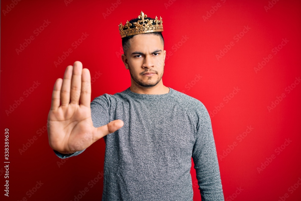 Φωτογραφία Young handsome man wearing golden crown of prince over isolated red background doing stop sing with palm of the hand