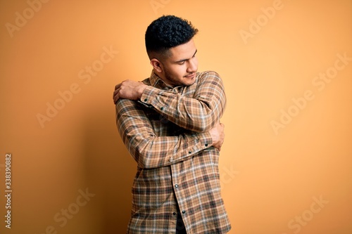 Young handsome man wearing casual shirt standing over isolated yellow background Hugging oneself happy and positive, smiling confident. Self love and self care © Krakenimages.com