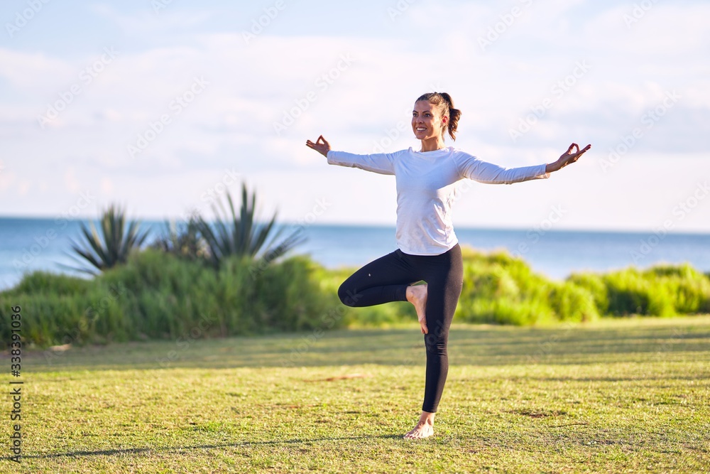 Young beautiful sportwoman smiling happy practicing yoga. Coach with smile on face teaching tree pose at park