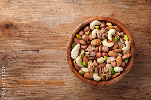 Wooden bowl with mixed nuts on rustic table top view. Healthy food and snack.