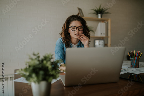 Portrait of young woman with glasses working on laptop at office. Office concept.