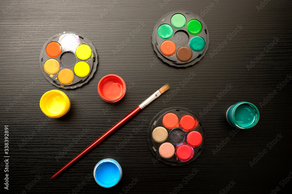Color paints and an paintbrush on black wooden background. 