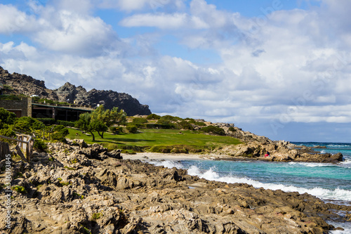 Amazing view on the coast and sea in La Pelosa Beach. Rocks, waves with foam and blue sky with clouds in Stintino, Sardinia, Italy