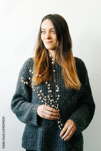 a smiling Girl in a gray knitted sweater holds natural branches of a budding willow in her hands.Minimal style.Easter concept