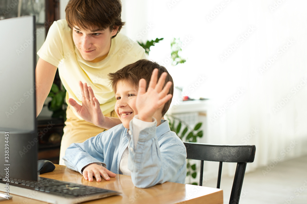 Smiling boy and teenager chatting online and waving at the computer screen. Quarantine and self-isolation due to coronavirus. Smiling boy and teenager chatting online and waving at the computer screen. Quarantine and self-isolation due to coronavirus.