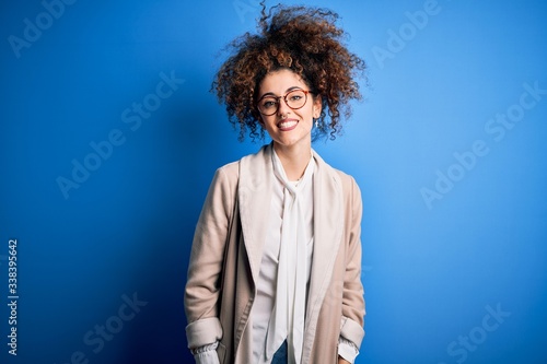 Young beautiful businesswoman with curly hair and piercing wearing jacket and glasses with a happy and cool smile on face. Lucky person.