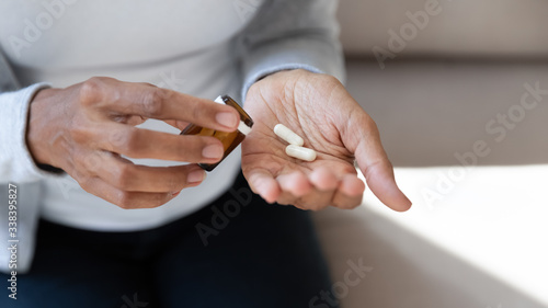 Black girl hold white pills and jar in her hands. Concept of healthcare and medicine, patient take daily dose of prescribed medicament, feel sick, antibiotics, painkillers or antidepressants. Close up photo