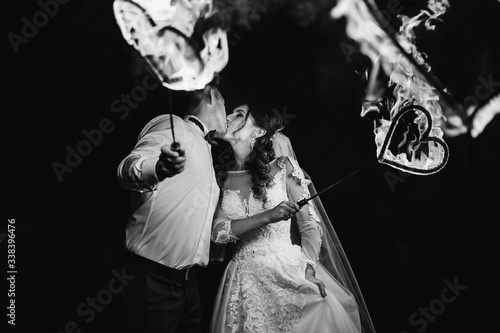 newlyweds kissing and holding a metal heart in the fire on black