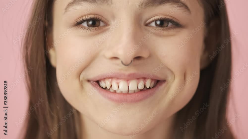 Close up view of playful pretty brunette woman in overalls posing and looking at the camera over pink background Close up view of playful pretty brunette woman in overalls posing and looking at the camera over pink background