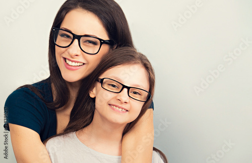 Happy young toothy mother and smiling kid in fashion glasses hugging on light blue background with empty copy space for text. Closeup