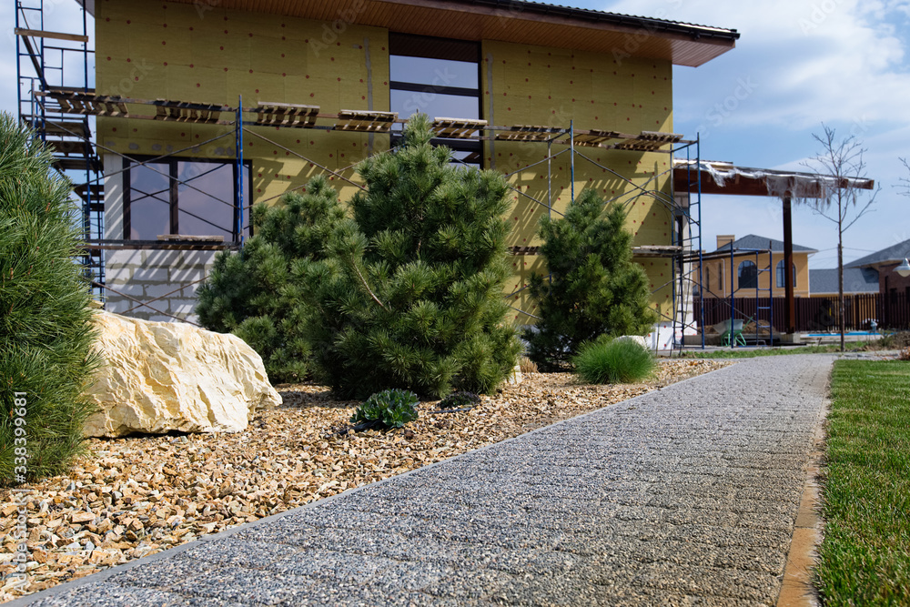 Modern conifer tree garden design. House under construction. Pavement path of the garden