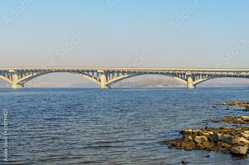 Scenic spring morning landscape photo of Metro bridge across Dnipro River in Kyiv. The bridge is used for metro and for automobile traffic. Cityscape in the morning smog in the background