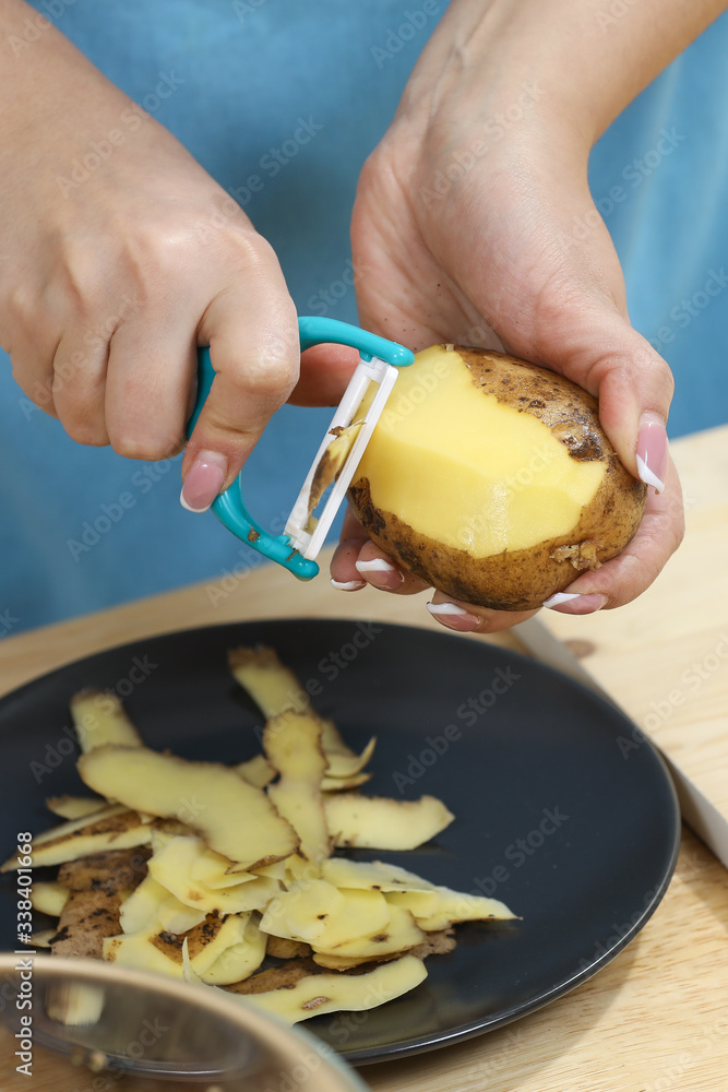 Young woman cooking in kitchen. Housewife preparing vegetables for cooking. Peel potatoes. Cooking soup