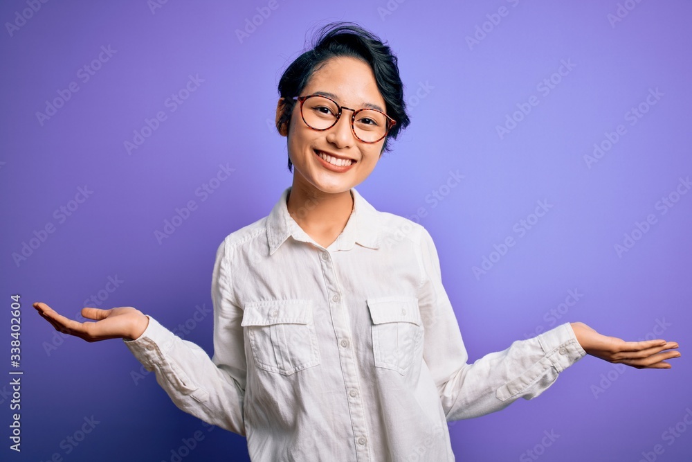 Young beautiful asian girl wearing casual shirt and glasses standing over purple background smiling showing both hands open palms, presenting and advertising comparison and balance Young beautiful asian girl wearing casual shirt and glasses standing over purple background smiling showing both hands open palms, presenting and advertising comparison and balance